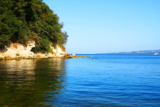 rocky coast overgrown with forest reflected in sea water.