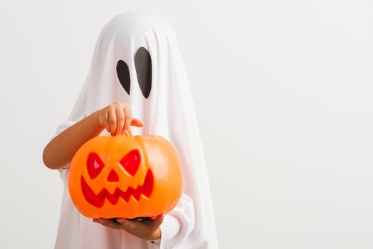 Funny Halloween Kid Concept, little cute child with white dressed costume halloween ghost scary he holding orange pumpkin ghost on hand, studio shot isolated on white background