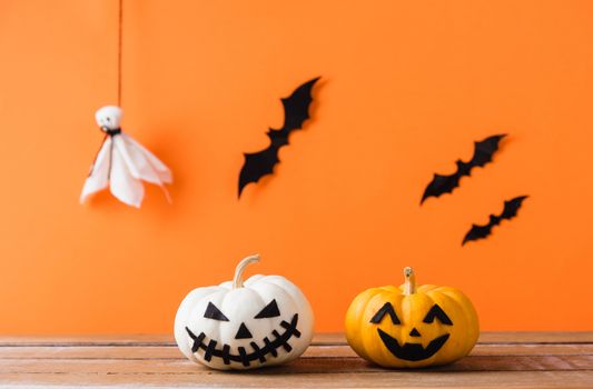 Funny Halloween day decoration party, Cute pumpkin ghost spooky jack o lantern face, black spider and bats on wooden table, studio shot isolated on an orange background, Happy holiday concept