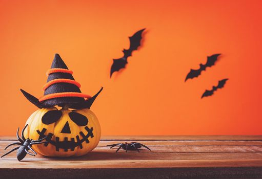 Funny Halloween day decoration party, Cute pumpkin ghost spooky jack o lantern face wear hat, black spider and bats on wooden table, studio shot isolated on an orange background, Happy holiday concept