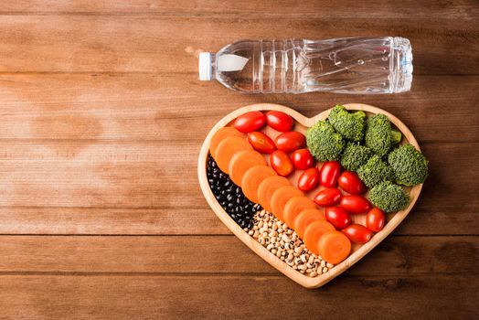 Top view of fresh organic fruits and vegetables in heart plate wood (carrot, Broccoli, tomato) and plastic water bottles on wooden table, Healthy lifestyle diet food concept