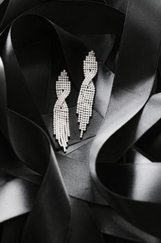 Luxury diamond earrings on black silk ribbon as background, jewelry and fashion brands