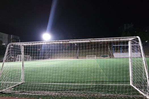 Night view of a soccer goal net under flood lights. Closeup view of goal net in a soccer playground