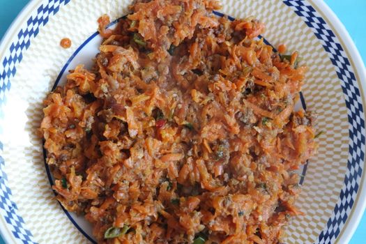 Top closeup view of a homemade dish made from carrot and vegetables served in a ceramic plate.