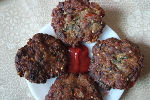 Delicious spicy fried round kebab served in white ceramic plate on a wooden floor with red sauce.