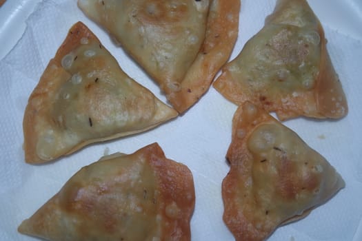 Closeup of delicious home made spicy and crunchy samosa pastries placed in a white ceramic plate on wooden floor