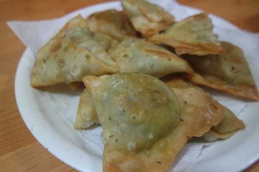 Closeup of delicious home made spicy and crunchy samosa pastries placed in a white ceramic plate on wooden floor