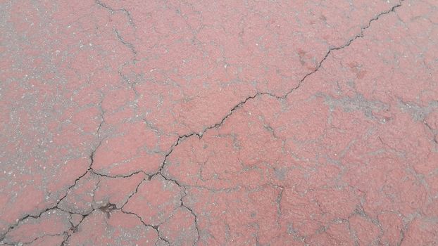 Red colored damaged road or paved pathway with crackes of different shpaes. Cracked texture with copy space for text and messages