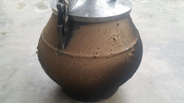 Pressure cooker covered with mud for cooking on fire. Cauldron type rural pressure cooker.