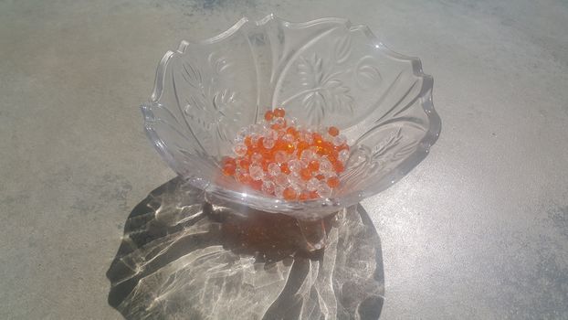 Shining, transparent, orange color crystal beads or gemstones or amber beads in a glass bowl over grey floor