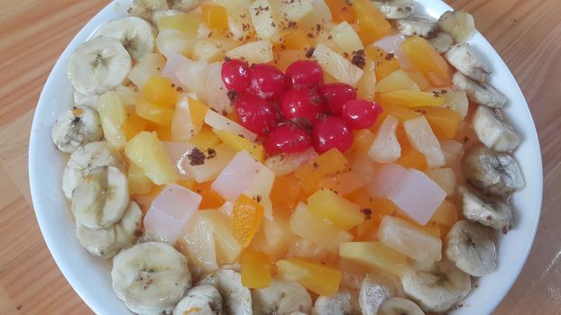 Creamy tasty sweet fruit trifle over custard with banana slices layered on surface on wooden floor. A top view of home made fruit trifle, a products for dessert after meal.