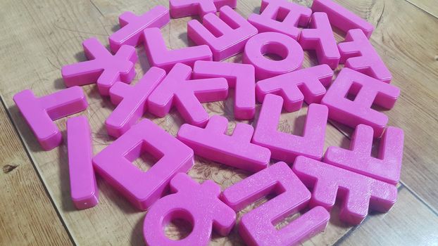 Set of plastic alphabet letters placed on a wooden floor. Alphabet set is used for educating children to learn words and language