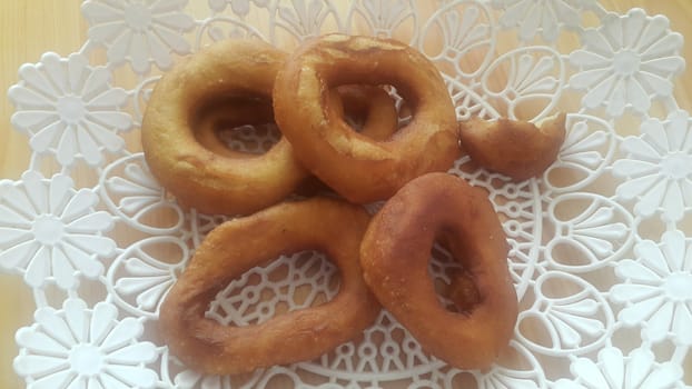 Closeup view of a set of freshly prepared donuts served on white changair. Donuts are placed in a changair over wooden floor