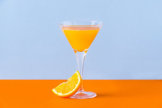 Fresh orange juice in a glass with a slice at the base on an orange surface and a light blue background