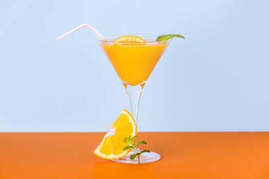 Fresh orange juice with a slice and a mint leaf at the base on an orange surface and a light blue background