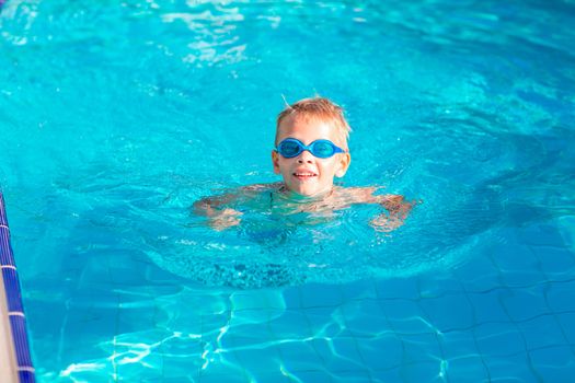 Cute happy little boy in goggles swimming and snorking in the swimming pool