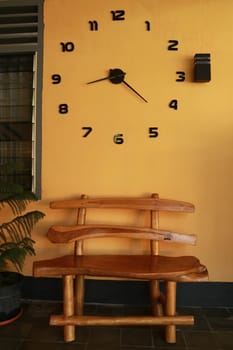 wooden bench near yellow wall. Vintage wooden bench under the wall clock.