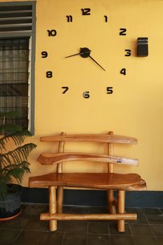 wooden bench near yellow wall. Vintage wooden bench under the wall clock.