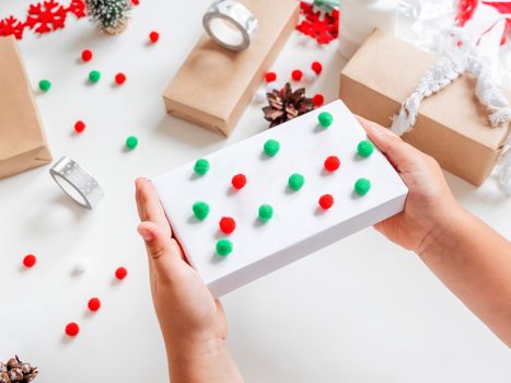 Kid wraps handmade Christmas presents in craft paper with colorful pompons and snowflake ribbons. Child prepares gifts for New Year celebration. Peaceful leisure activity before winter holidays.