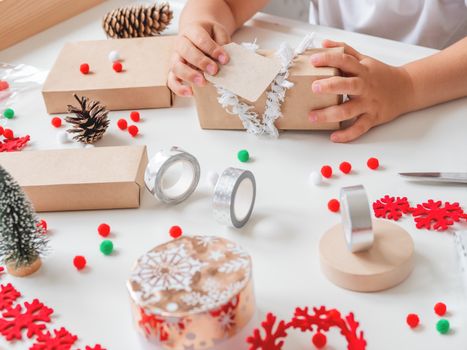 Kid wraps handmade Christmas presents in craft paper with colorful pompons and snowflake ribbons. Child prepares gifts for New Year celebration. Peaceful leisure activity before winter holidays.