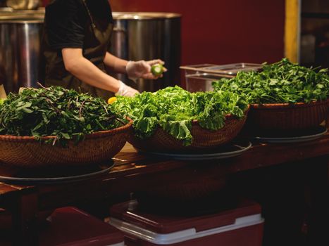 Chef cooks something tasty in Vietnamese restaurant. Wicker baskets with herbs for Asian cuisine. Mint, lime, pepper, lettuce.