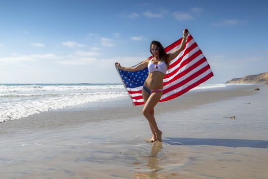 A gorgeous brunette model poses with an American Flag At The Beach