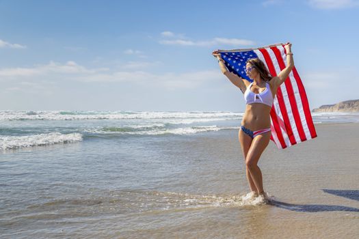 A gorgeous brunette model poses with an American Flag At The Beach