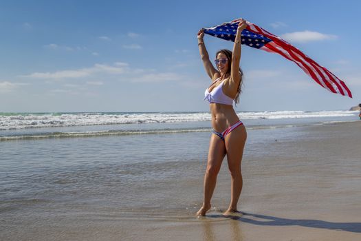 A gorgeous brunette model poses with an American Flag At The Beach