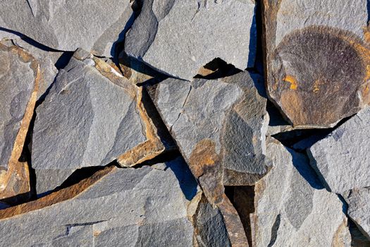 Texture and background of large chunks of rocky gray sandstone with rifts and rusty spots in harsh sunlight.