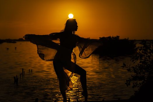 A beautiful latin model is silhouetted as she poses with the rising sun behind her on a exotic Caribbean beach