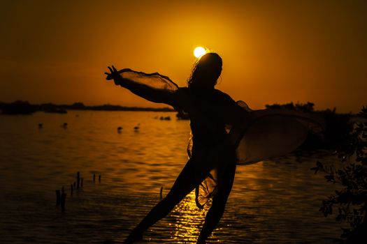 A beautiful latin model is silhouetted as she poses with the rising sun behind her on a exotic Caribbean beach