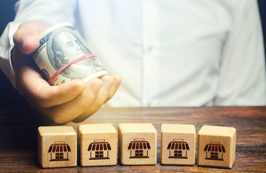 Blocks symbolizing business network and businessman holds out money. Offer for purchase of a business. Merge small competitors, expansion empire. Market monopolization. Franchise concept.