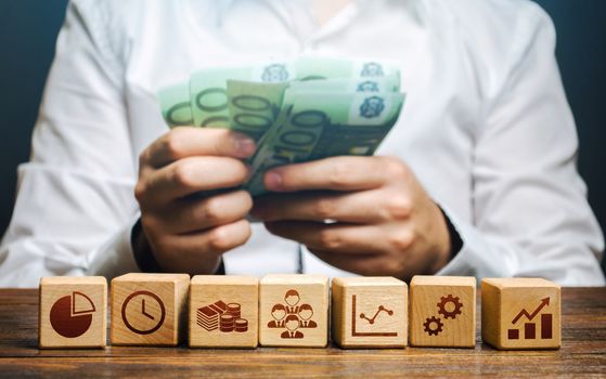 A man is counting money and blocks with business attributes. Good business model. Profitability. The rules for successful investment. High performance, great work. Company management