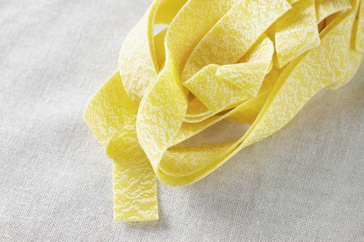 Dry pasta pappardelle on white cotton cloth ,delicious yellow  large flat pasta noodles 