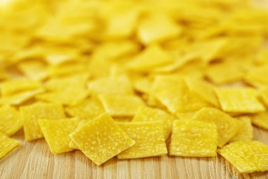 Pile of small flat squares of egg pasta called quadrucci on wooden background,yellow color pasta with rough surface 