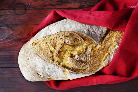 Freshy baked loaf of bread wrapped in red cotton cloth on dark wooden table , beautiful bread crust  ,durum wheat bread