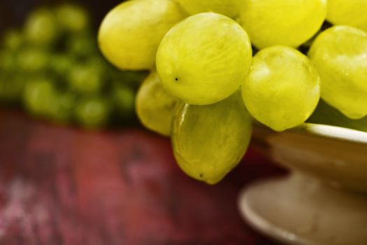 Bunch of green grapes in a fruit bowl on  colored table  , in the background grapes out of focus , the fruits are bright and wet