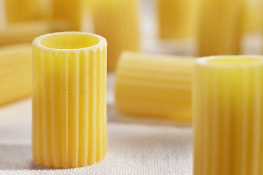 Italian pasta called mezzi rigatoni on white cotton cloth ,tube-shaped pasta with ridges down their lenght ,studio shot
