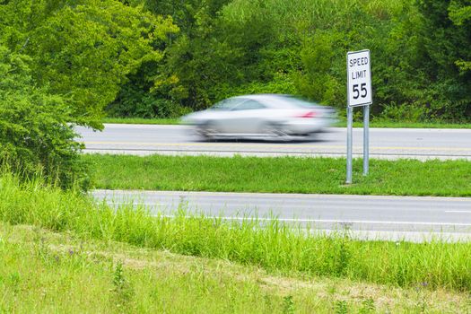 Horizontal shot of a speeding car streaking by a speed limit sign.  Blurring shows motion.