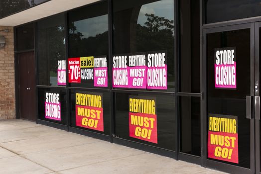 Horizontal angled shot of the windows of a store plastered with going out of business signs due to the pandemic.