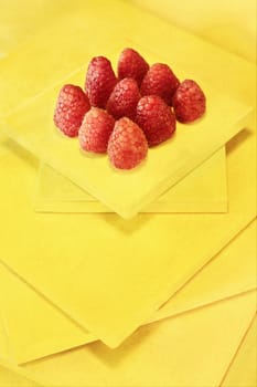 Group of fresh red raspberries on yellow abstract background , bright  ripe red fruits ready to eat