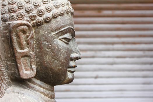 Closeup of side view of Gautaum Buddha statue in front of closed shutter 