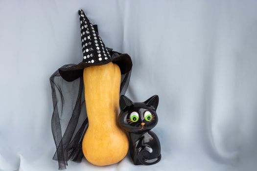 Happy Halloween. A black cat toy hides behind a pumpkin in a witch's hat.