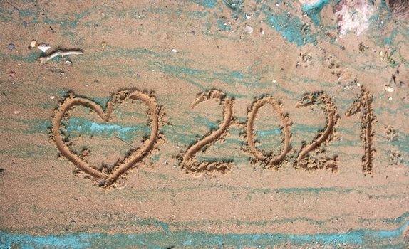 The concept of a New year. Heart and numbers 2021 in the sand. Summer beach holidays . The message is handwritten.