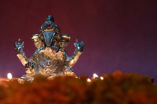 oil lamp illuminated in front of lord ganesha idol with flowers and space for text 