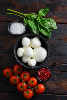 Raw ripe Mozzarella cheese balls with fresh basil leaves and cherry tomatoes, the ingredients , on old wood background top view vertical.