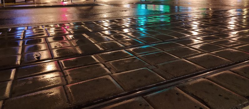 pavement wet from the rain with reflective lights in the evening.