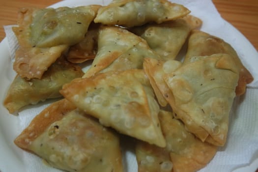 Closeup of delicious home made spicy and crunchy samosa pastries placed in a white ceramic plate on wooden floor