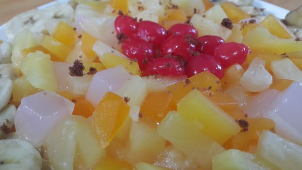 Creamy tasty sweet fruit trifle over custard with banana slices layered on surface on wooden floor. A top view of home made fruit trifle, a products for dessert after meal.