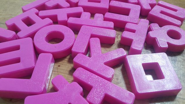Set of plastic alphabet letters placed on a wooden floor. Alphabet set is used for educating children to learn words and language